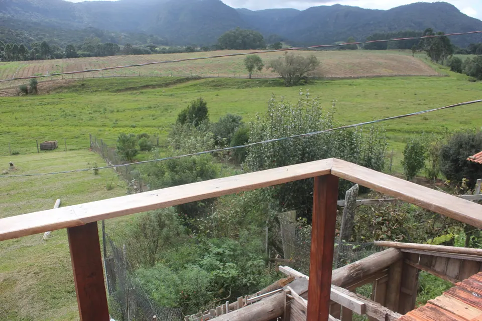 Vale verde com lavouras e as montanhas da serra ao fundo, visto de um deck de madeira